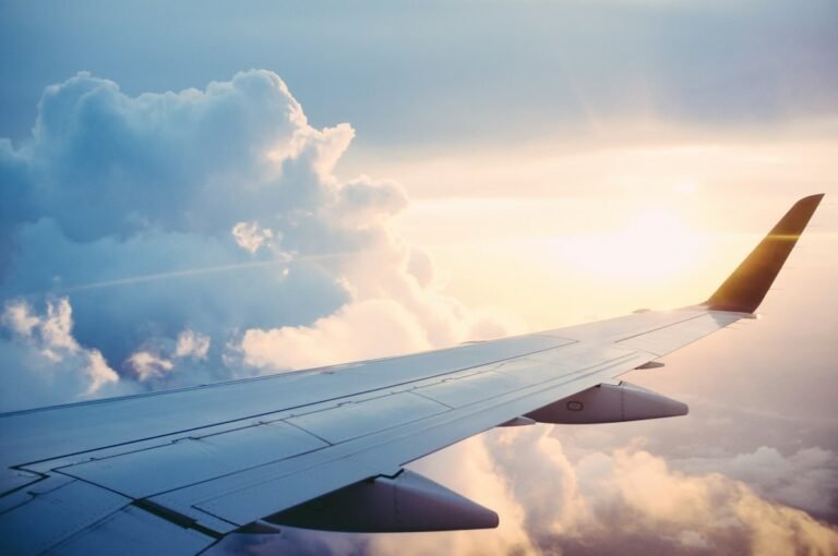 Commercial passenger jet wing flying above white clouds at sunrise